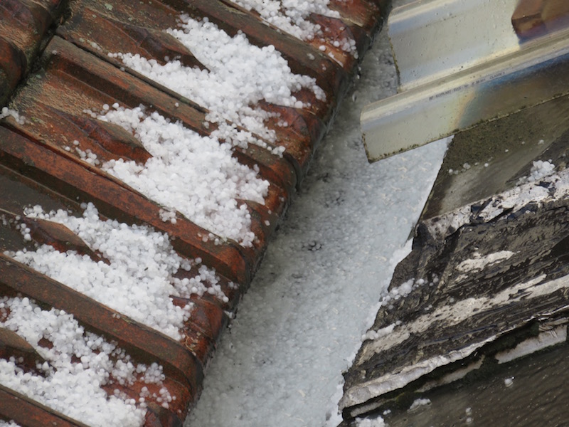 Hail stones collect and flow along the gutter.