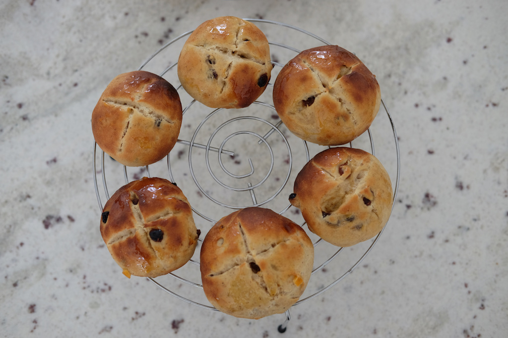 Ring of hot cross buns cooling on a rack.